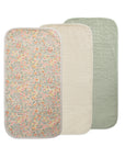 Three Mushie Changing Pad Liners are shown overlapping: one with a floral print, one in solid cream, and one in solid sage green. Each liner has rounded corners and a soft, quilted organic cotton texture.