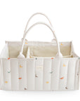 Mushie Diaper Caddy: white quilted organizer with handles, colorful dinosaur print.