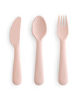 The mushie Dinnerware Cutlery Set features a light pink knife, spoon, and fork made from non-toxic plastic, arranged side by side on a white background—ideal for everyday use.