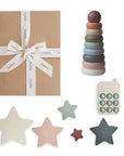 The mushie Everyday Play Gift Set ($48 value) includes a brown gift box with a white ribbon, stackable pastel rings, a toy phone, and five star-shaped sensory toys—perfect for supporting baby's fine motor skills.