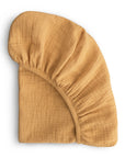 The mushie Extra Soft Bassinet Muslin Crib Sheet in mustard yellow features textured, breathable baby bedding. Neatly folded with one elasticized corner partially visible, it’s shown on a white background.
