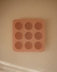The Mushie Baby Food Freezer Tray is a peach-colored, BPA-free silicone tray with nine round, raised buttons arranged in a 3x3 grid and features a square design.