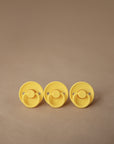 Two FRIGG Rope/Daisy Silicone Pacifiers in Sunflower and Fuchsia (6-18 Months) are displayed on a beige surface—high-quality, medical-grade essentials for your little one. Comes as a 2-pack from FRIGG.