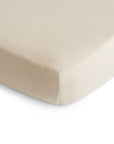 Close-up of the corner of a mushie Stretchy MINI Crib Sheet in beige, snugly fitted on a mattress, highlighting its smooth, breathable organic cotton fabric and soft look with clean lines.
