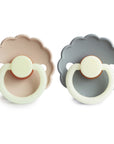 The FRIGG Daisy Night Natural Rubber Pacifier 2-Pack includes two pacifiers—one beige, one light gray—with scalloped edges, round handles, circular shields, and natural rubber latex nipples for comfort.