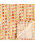 The mushie Organic Cotton Muslin Swaddle Blanket in Happy Flowers Check features a retro geometric pattern of orange, yellow, white, and light blue squares with a white flower motif. One corner is folded up to show the reverse side.