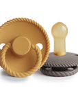 The Mushie FRIGG Rope Natural Rubber Pacifier 2-Pack includes mustard yellow and gray pacifiers with rope-patterned edges, round handles, and natural rubber latex nipples. The brand name FRIGG appears on the yellow pacifier.