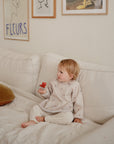 Toddler in a mushie Long Sleeve Bib eats a strawberry on a white couch with art behind.