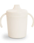 The Mushie Trainer Sippy Cup is a cream, non-toxic sippy cup with easy-grip handles, a spout lid, and an embossed Mushie logo on the front for added style.
