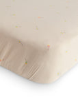 A close-up of the mushie Extra Soft Muslin Crib Sheet, featuring a subtle pastel kite pattern on light beige, shown fitted over a mattress corner for gentle, breathable baby bedding.