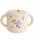 The mushie Snack Cup in Lilac Flowers features a beige silicone body, two handles, a flexible slit lid, and a blue floral pattern—making it the perfect spill-proof option for mess-free toddler snacking.