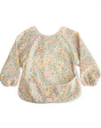 The mushie Long Sleeve Bib in Pastel Blooms features a water-resistant design, elastic neckline and cuffs, an all-over floral print, and a front pocket to catch food. Wipe-clean convenience keeps your little one tidy at every meal.