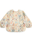 The mushie Long Sleeve Bib in Space features a colorful, pastel space-themed pattern, elastic cuffs, water-resistant material, a wipe-clean surface, and a handy bottom pocket—perfect for kids.