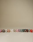 FRIGG Daisy Natural Rubber Pacifier 2-Pack in assorted colors on a light beige background.