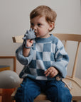 Toddler bites a mushie No-Drop Teether shaped like a dinosaur.
