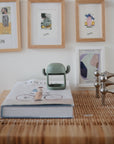 A book and decor on a table with a mushie No-Drop Teether and framed art in the background.
