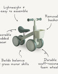 Mushie Mini Toddler Bike in green and white with labeled features and a removable basket.