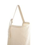 The mushie Muslin Nursing Cover is a cream-colored tote bag with a single shoulder strap and minimalist design, made from breathable organic cotton, photographed on a white background.