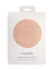A white box with a round window displays a peach muslin nursing cover inside. The mushie brand name and Muslin Nursing Cover details are printed on the front.