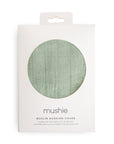 A white box with a circular window displays a light green, breathable Muslin Nursing Cover by mushie. The label features the product name in English, Spanish, and French.