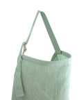 A light green linen tote bag with a wide strap and minimalist design, ideal for carrying the mushie Muslin Nursing Cover, photographed on a white background—perfect for parents on the go.