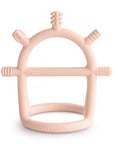 The mushie No-Drop Sensory Teether is a pale pink silicone arch with five textured knobs, designed to soothe teething discomfort and provide gentle relief for babies.