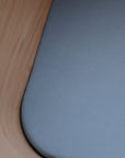 Close-up of a smooth, curved wooden edge beside a light blue mushie Mini Muslin Crib Sheet, made from 100% breathable cotton. The wood features a light, natural finish—likely the corner of a crib.