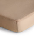 Close-up of the corner of a mushie Mini Muslin Crib Sheet, neatly fitted on a mattress with a smooth, wrinkle-free surface, set against a white background.