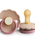 The FRIGG Daisy Natural Rubber Pacifier 2-Pack | Limited Edition by FRIGG includes two beige and pink scalloped pacifiers—one showing the ring handle, the other revealing its natural rubber latex nipple for comfort.