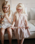 Two young girls smile on a white couch, holding the colorful mushie HEX Connect Building Toy Set—an engaging activity that sparks creativity and spatial reasoning.