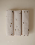Three rolled beige Changing Pad Liners by Mushie, made from organic cotton with a subtle bee pattern, are arranged side by side on a light background—ideal as soft muslin liners for your diaper changing pad.