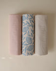 Three Mushie Changing Pad Liners are displayed side by side: one in pale pink, one cream, and one white with a blue floral design.