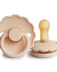 The FRIGG Daisy Natural Rubber Pacifier 2-Pack Limited Edition in Pink Cream shows two pacifiers with scalloped edges—one displaying the handle and one upright to reveal the natural rubber latex nipple.