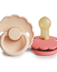 The FRIGG Daisy Natural Rubber Pacifier 2-Pack features two daisy-shaped pacifiers in pink and beige, each with scalloped edges, round handles, natural rubber latex nipples, and the FRIGG brand name on the front.