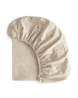 The mushie Stretchy MINI Crib Sheet, made from breathable organic cotton, features a beige color with small brown rainbow patterns and an elastic edge. It is neatly folded against a white background.