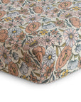 A close-up of mushie’s Extra Soft Muslin Crib Sheet, featuring a colorful floral pattern of pink, orange, white, and yellow flowers with green leaves on a light background—perfect breathable bedding for babies.