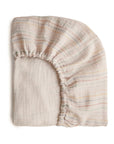 The mushie Extra Soft Muslin Crib Sheet is a light, breathable baby bedding with elastic edges and subtle pastel stripes, shown folded on a white background.
