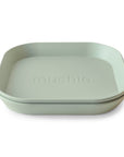 Two stacked light green, square-shaped mushie Square Dinnerware Plates with rounded corners; the top plate has "mushie" embossed in the center. This BPA-free set is safe and stylish for little ones.