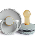 The Mushie FRIGG Rope Natural Rubber Pacifier 2-Pack includes two light gray pacifiers with rope-like edging—one displays the natural rubber latex nipple, and the other stands upright, showing its handle and embossed FRIGG logo.