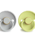 The Mushie FRIGG Rope Natural Rubber Pacifier 2-Pack includes light gray and light yellow pacifiers with rope-edge design, round handles, and embossed branding. Features natural rubber latex nipples—perfect baby essentials.