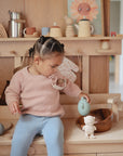 Toddler with wooden toys and a FRIGG Daisy Natural Rubber Pacifier by FRIGG at a play kitchen.