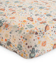 The mushie Extra Soft Muslin Crib Sheet features a colorful space-themed pattern with rockets, planets, stars, and moons in orange, blue, yellow, and green on white—perfect breathable bedding for babies.