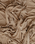 The mushie Stretchy Swaddle in beige features breathable, soft fabric with a textured, layered look from natural folds and creases—perfect for keeping your baby cozy and comfortable.