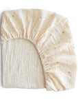 The mushie Extra Soft Muslin Crib Sheet in cream features a subtle crinkled texture and small gold sun designs, with elastic edges for a secure fit—breathable and stylish bedding for your baby.