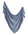 A light blue mushie Stretchy Swaddle with gentle folds and ruffled edges drapes softly in a flowing curve, resembling a breathable baby blanket against a white background.