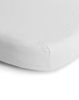 Close-up of the corner of a mushie Mini Muslin Crib Sheet covering a mattress, highlighting its smooth 100% cotton muslin fabric and snug fit. The background is plain white.