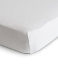 Close-up of a neatly made bed with the mushie Stretchy MINI Crib Sheet in white, showing one corner tightly wrapped around the mattress for a secure, breathable fit.