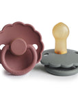 The FRIGG Daisy Natural Rubber Pacifier 2-Pack by FRIGG features two daisy-shaped pacifiers, one in mauve with a ring and one in gray with a tan natural rubber latex nipple, both shown upright on a white background.