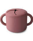 The mushie Snack Cup in Woodchuck is a spill-proof silicone toddler snack cup, designed with two side handles and a flexible, petal-shaped opening on top.