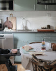 Modern kitchen with green cabinets, Danish Hygge style, and a mushie Stacking Rings Toy on the table.